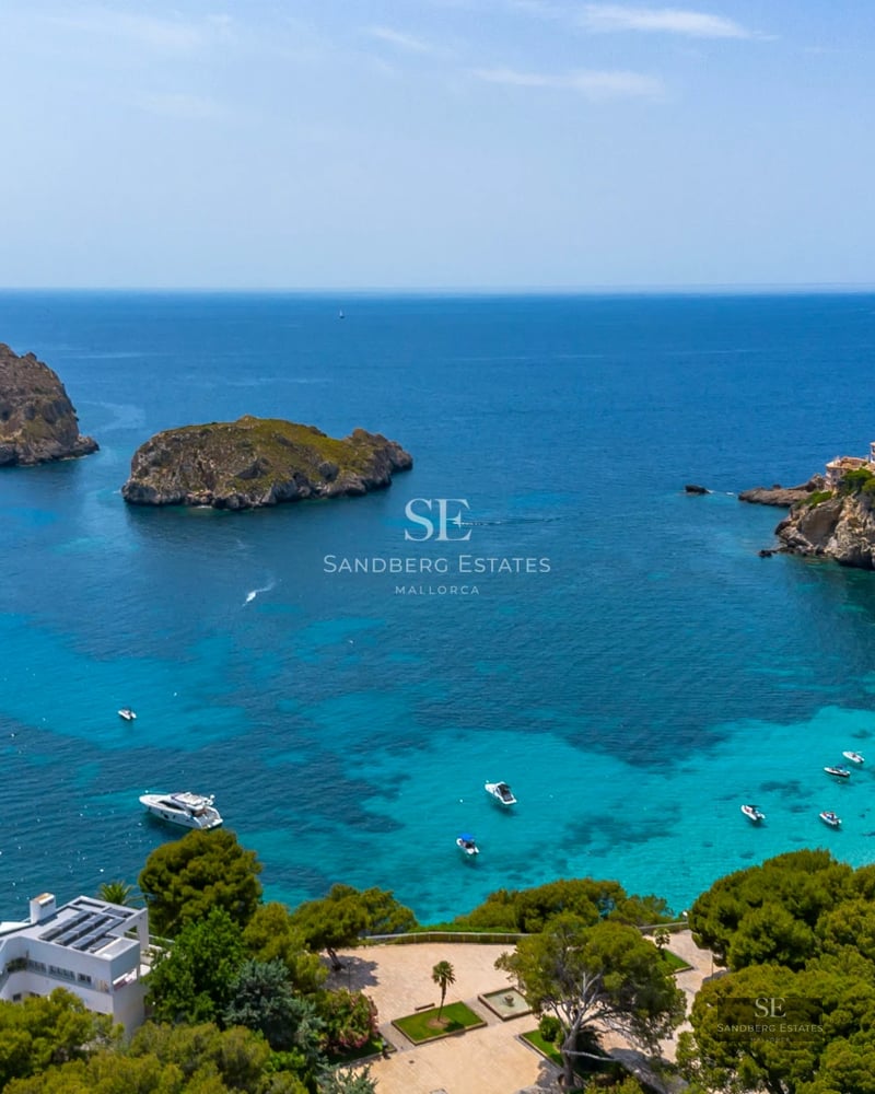 View of a luxurious infinity pool with stone edging, modern sun loungers, and lush greenery. Minimalist architecture, blue sky.