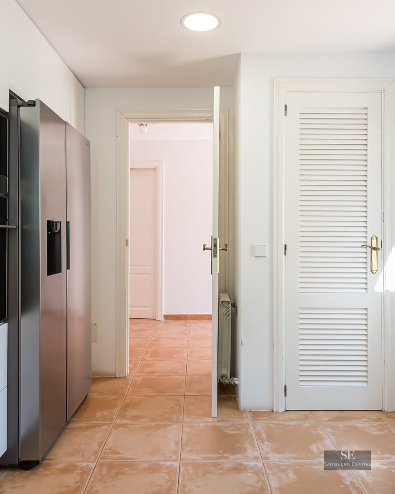 Bright kitchen with white cabinets, marble countertops, stainless steel fridge, and terracotta tile flooring.