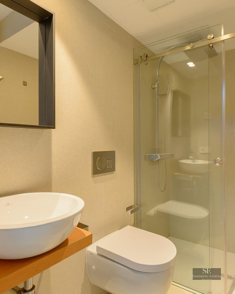 Contemporary bathroom featuring a white vessel sink on wood, wall-hung toilet, and a glass-enclosed walk-in shower.