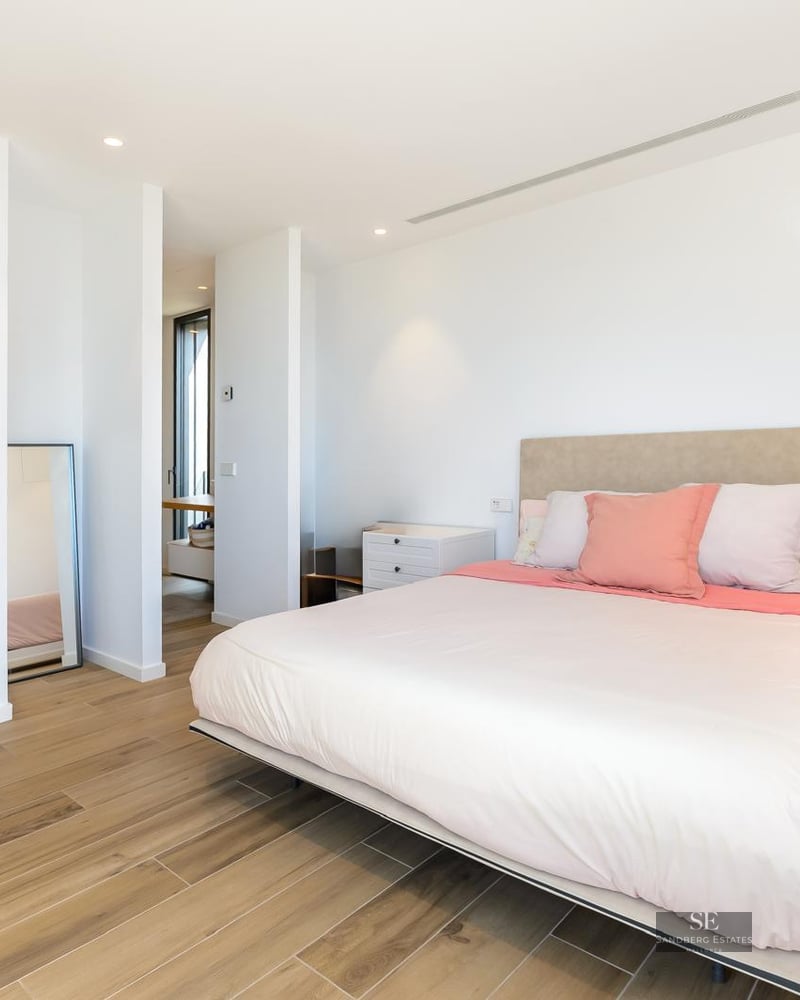 Bright, modern bedroom featuring a large bed with pink pillows, light wood floors, and white walls.