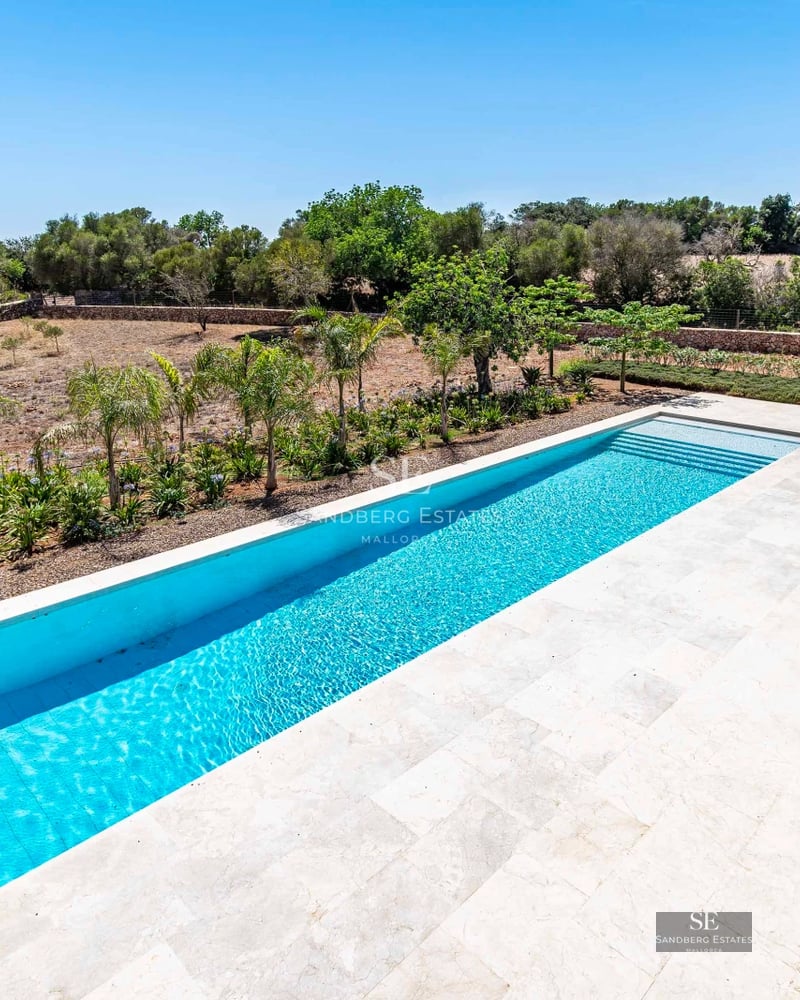 Bright, spacious living room with panoramic windows, light wood flooring, and modern designer furniture. Views of a lush garden.