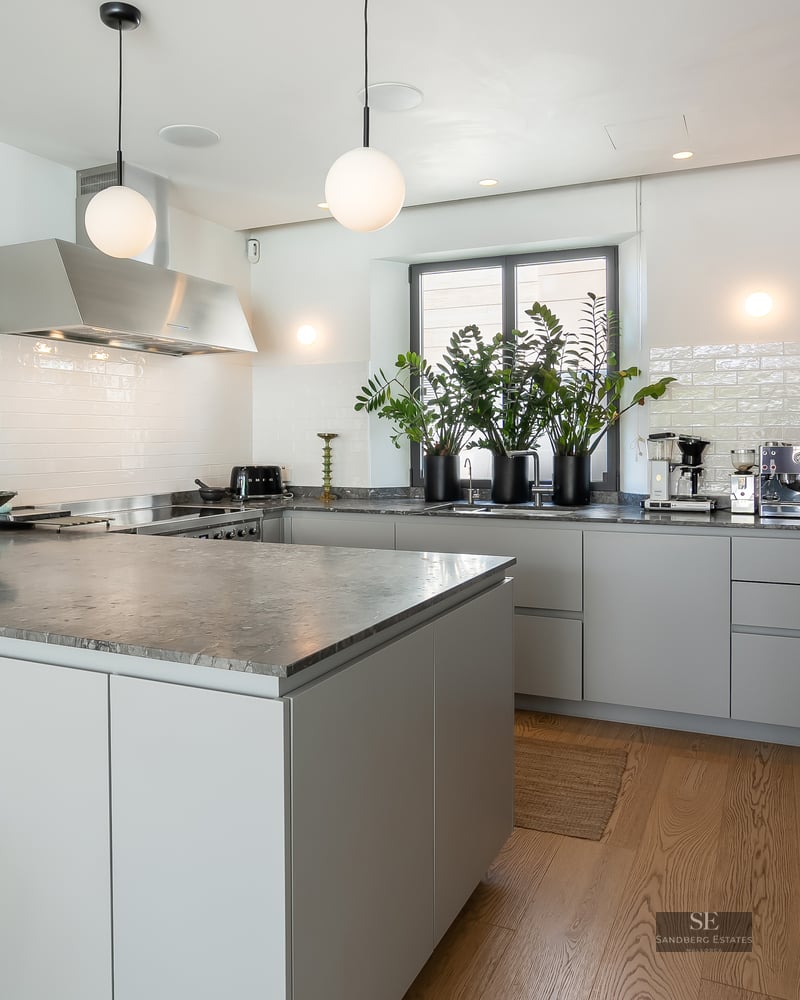 Contemporary kitchen featuring a large gray marble island, minimalist gray cabinetry, and white globe pendant lights.
