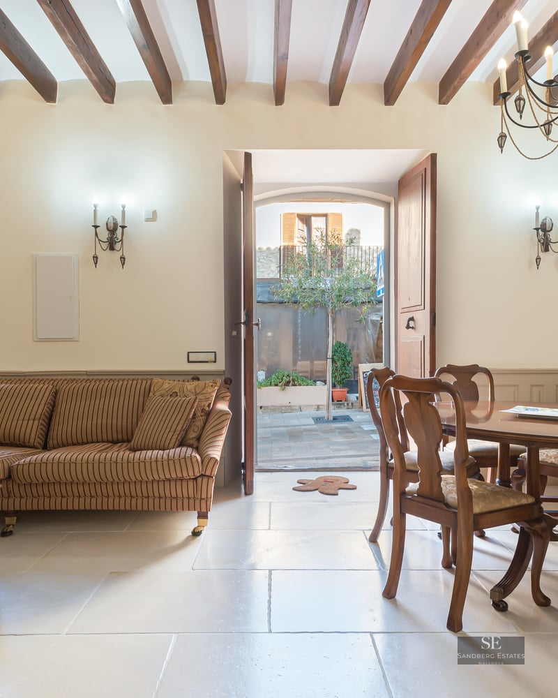 Rustic interior with a striped sofa, wooden dining table, stone floors, and exposed wooden ceiling beams.