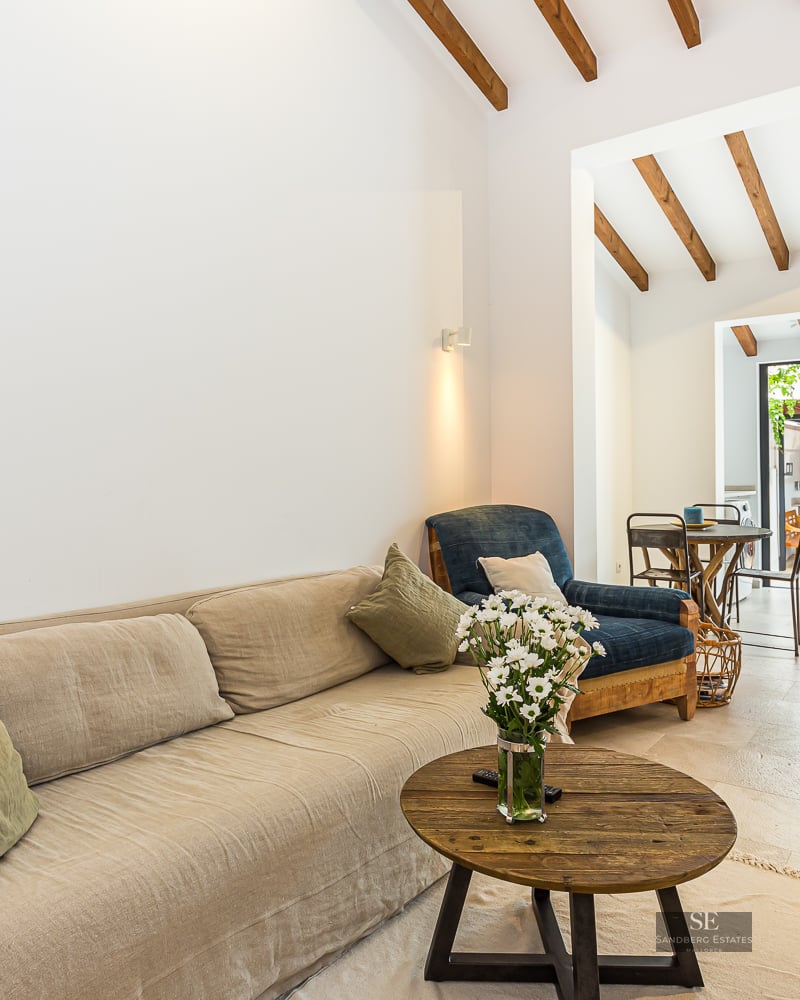Living room with a beige sofa, wooden coffee table, exposed ceiling beams, and glass doors opening to a patio.