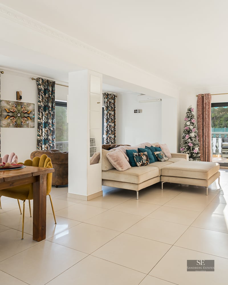 Espace de vie lumineux avec chaises en velours moutarde, canapé beige et grandes baies vitrées ouvrant sur une terrasse.