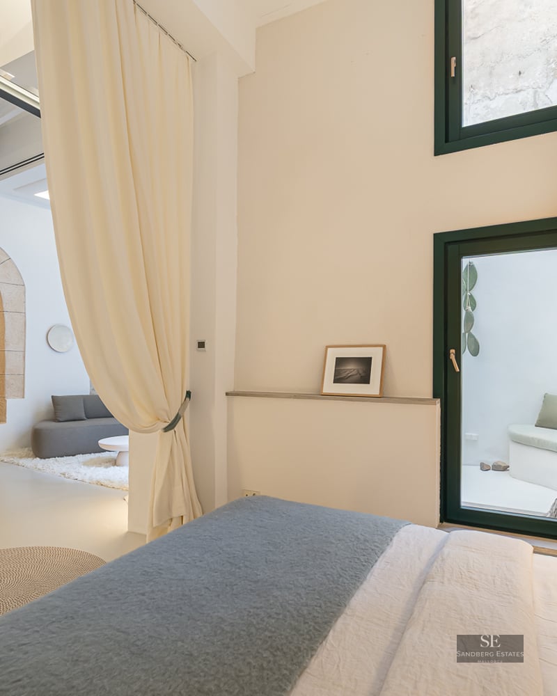 Bright master bedroom featuring floor-to-ceiling curtains, a stone arch, and a view into a modern lounge.