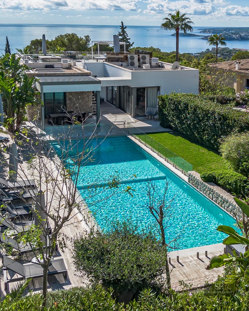 Grande piscine turquoise entourée d'un jardin luxuriant et d'une terrasse en bois avec vue panoramique sur la mer Méditerranée.