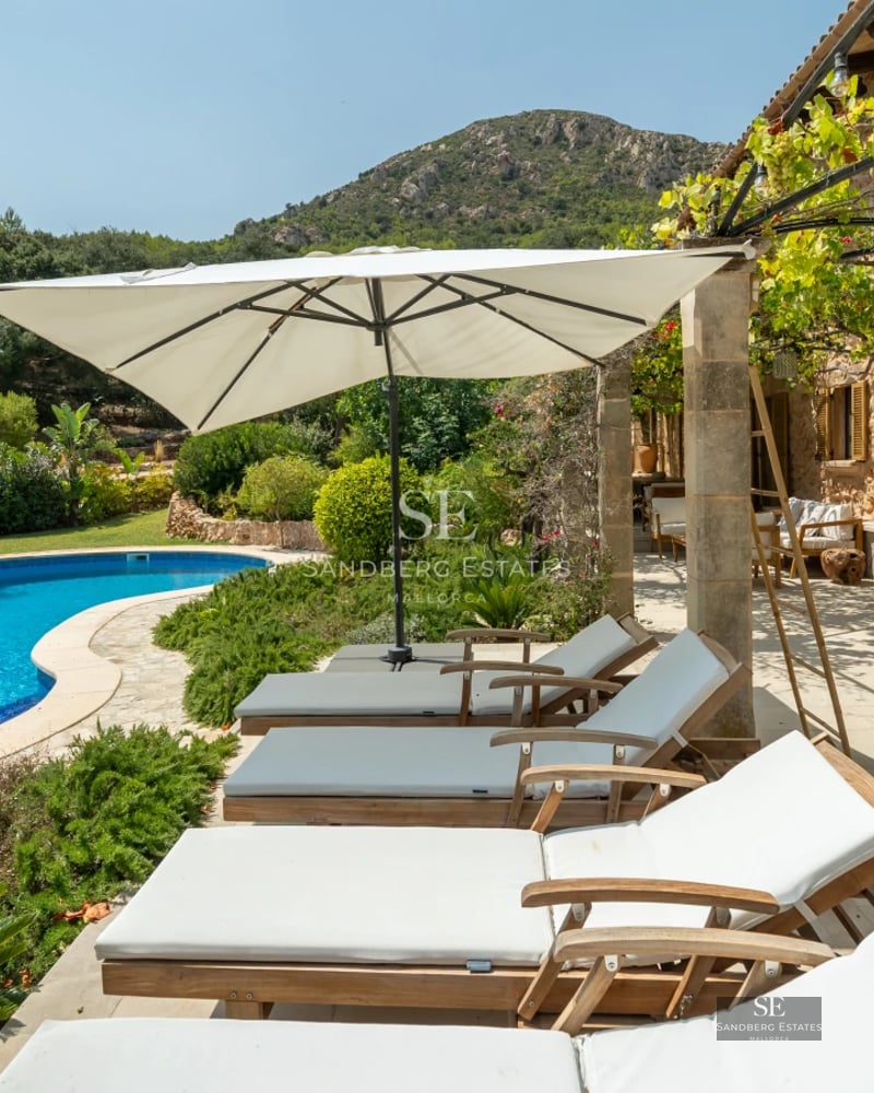 View of a modern villa's pool with outdoor seating area, lounge chairs, and lush gardens. Minimalist architecture with large windows.