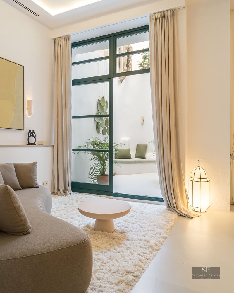 Modern living room with a curved sofa, shag rug, and large glass doors leading to a private white patio.
