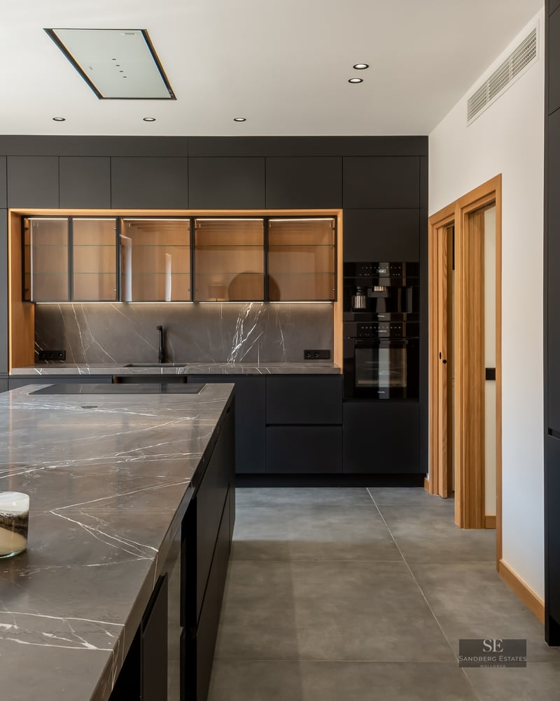 Modern kitchen featuring matte black cabinetry, grey veined marble countertops, and large windows.