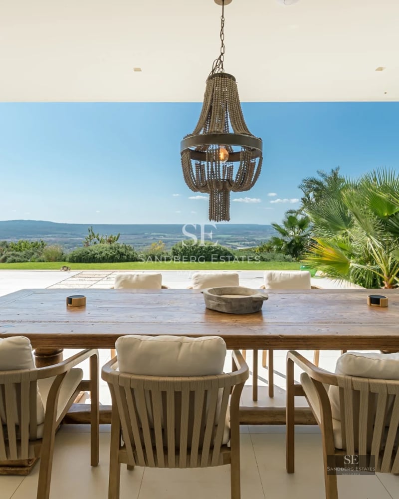 View of a modern pool surrounded by lush greenery and a house with large windows. Minimalist design.