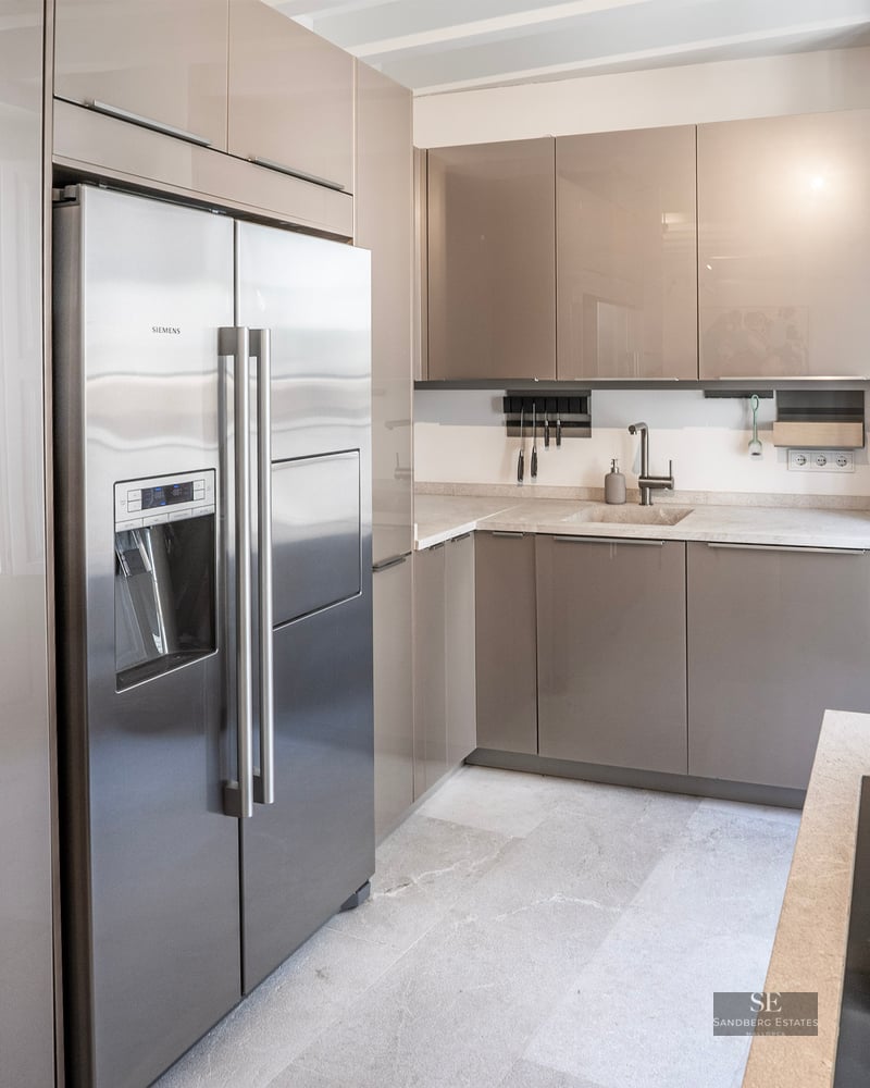 Cuisine moderne avec placards taupe brillant, réfrigérateur en acier inoxydable et plans de travail en pierre claire.