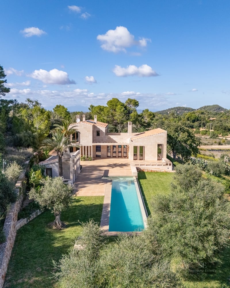 Aerial-style view of a modern stone villa with a long turquoise lap pool surrounded by lush Mediterranean trees.