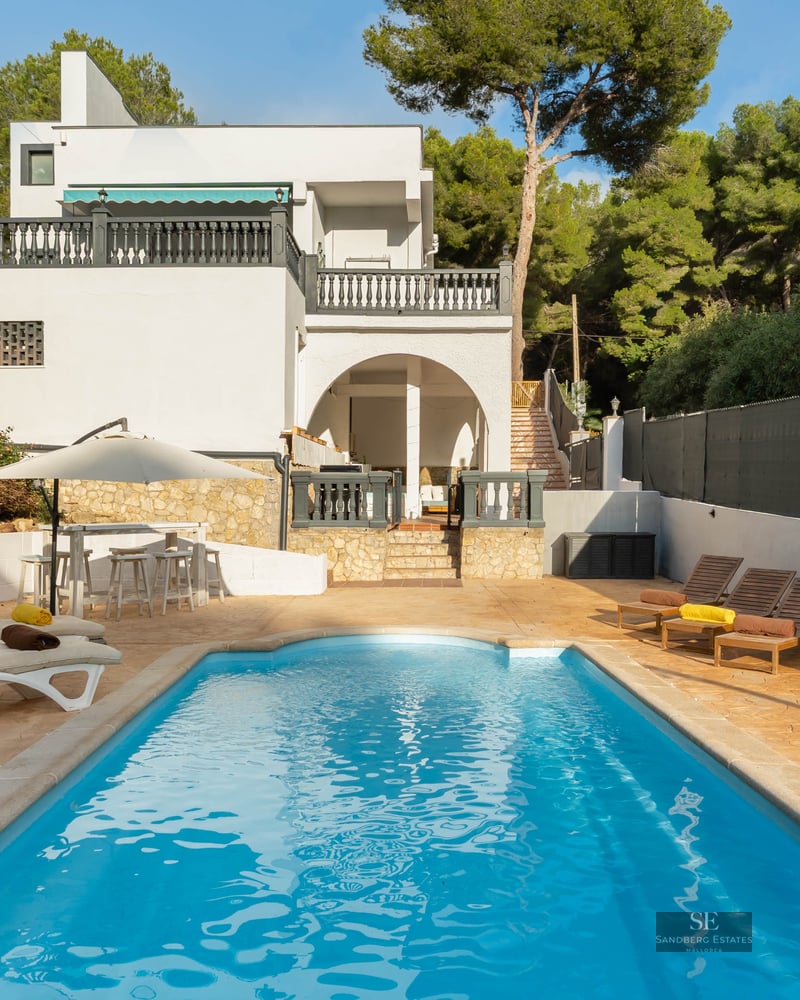 Piscine bleue entourée d'une terrasse en pierre avec transats et une villa blanche en arrière-plan.