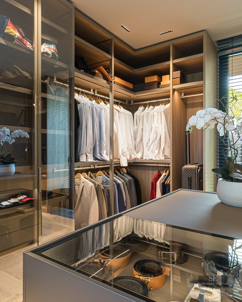 Spacious modern walk-in closet with wood shelving, glass display island, and designer clothes neatly organized.