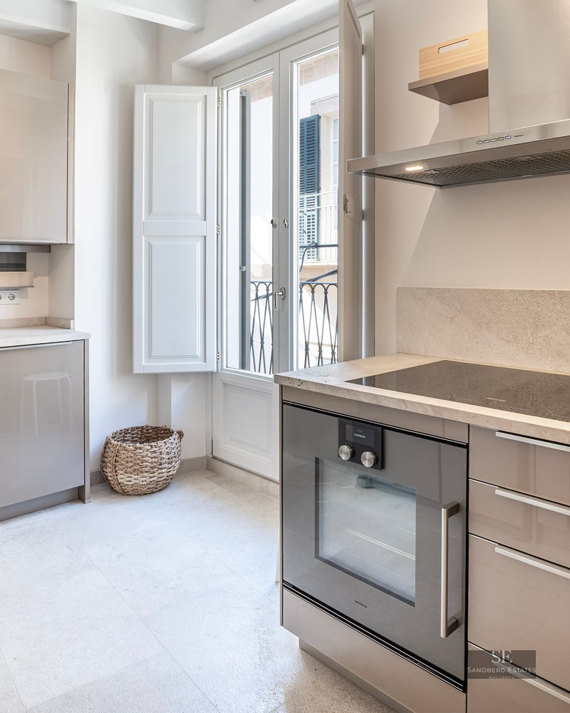 Cuisine moderne lumineuse avec placards beige brillant, plan de travail en pierre et porte-fenêtre.