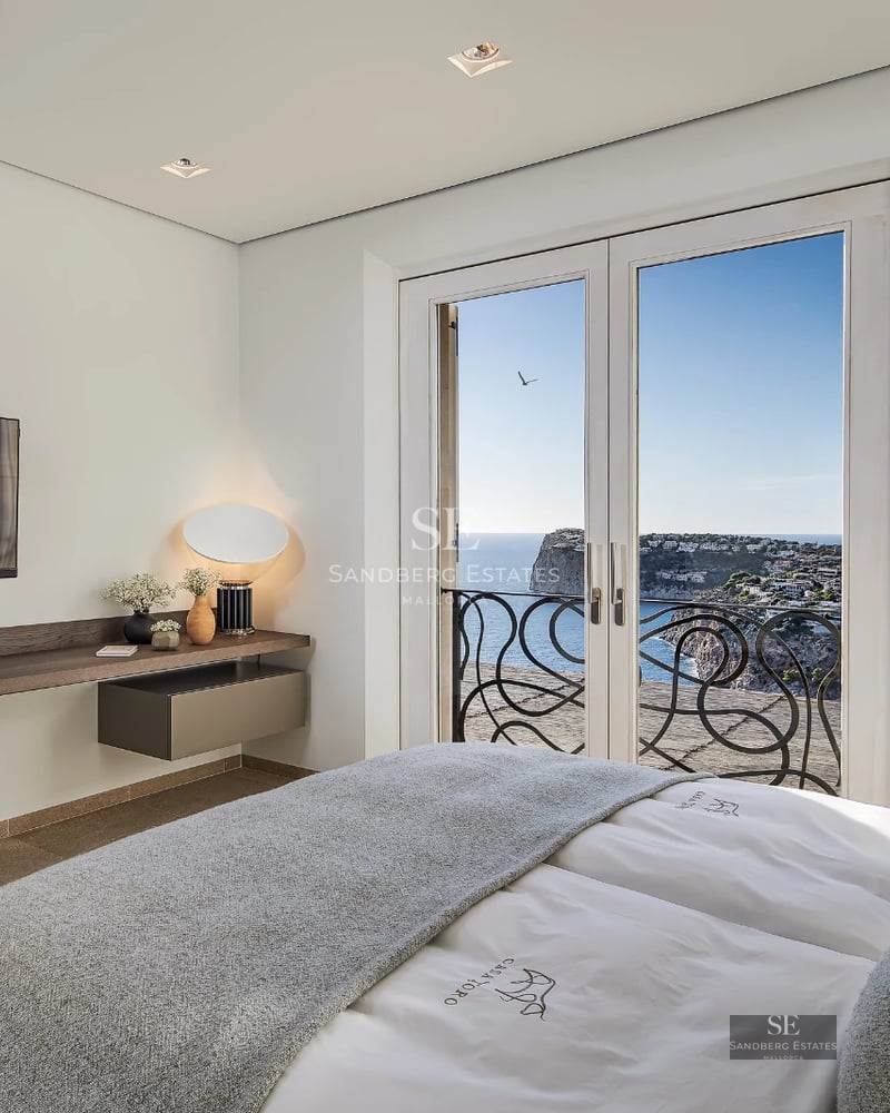 Spacious living room with window walls, beige sofa, light wood floor, designer rug, and panoramic sea view. Natural lighting.