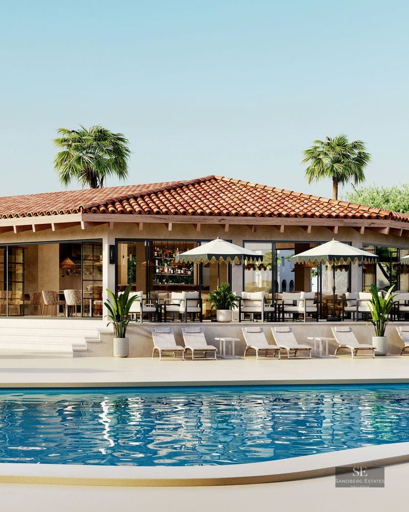 A wide turquoise swimming pool surrounded by white sunbeds and umbrellas in front of a Mediterranean pavilion with palms.