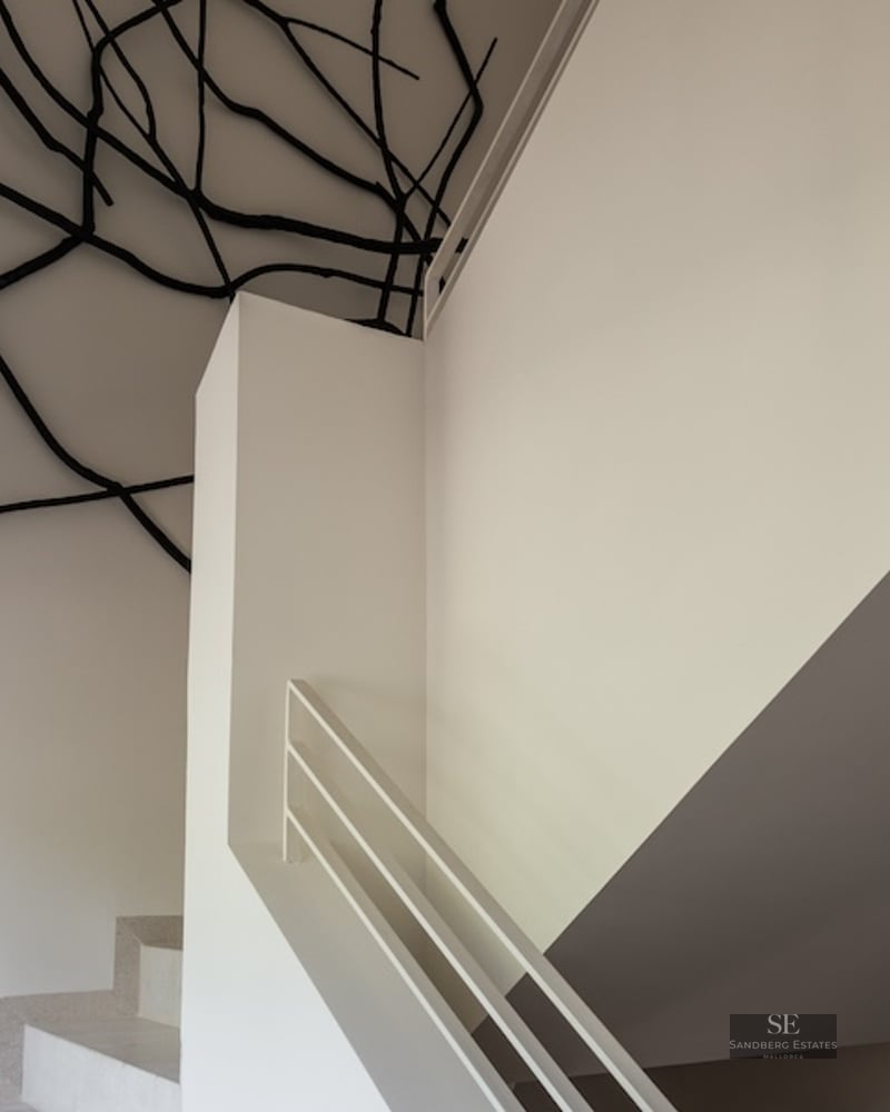 White minimalist staircase featuring a black branch-like art sculpture on the ceiling and walls in a bright, modern space.
