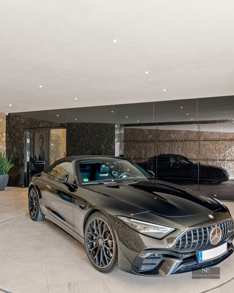 A black Mercedes sports car on a circular rotating platform in a modern garage with natural stone walls and mirrors.