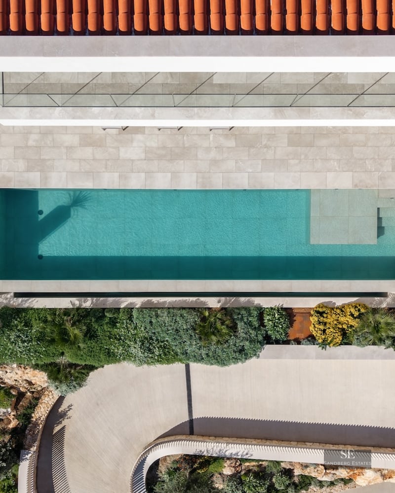 Bird's eye view of a turquoise swimming pool, stone terrace, terracotta roof, and lush Mediterranean landscaping.