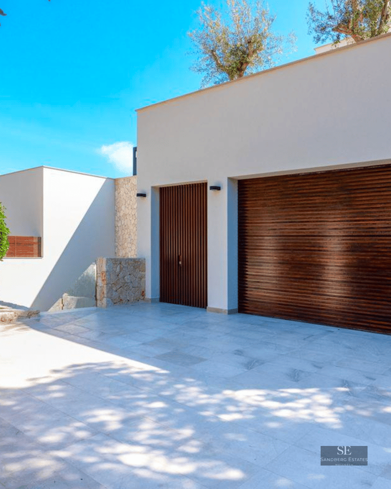 Spacious parking area with dark wood garage doors, natural stone walls, and blue sky.