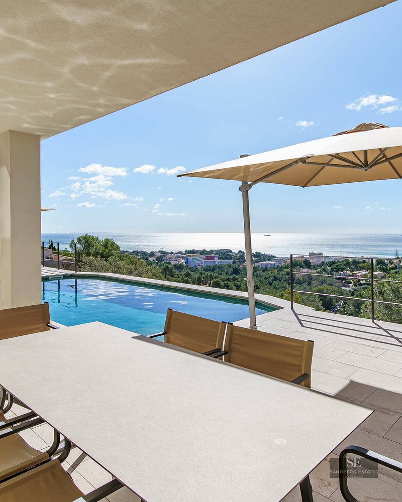 Spacious modern terrace with an infinity pool, dining area, and panoramic sea views under a clear blue sky.