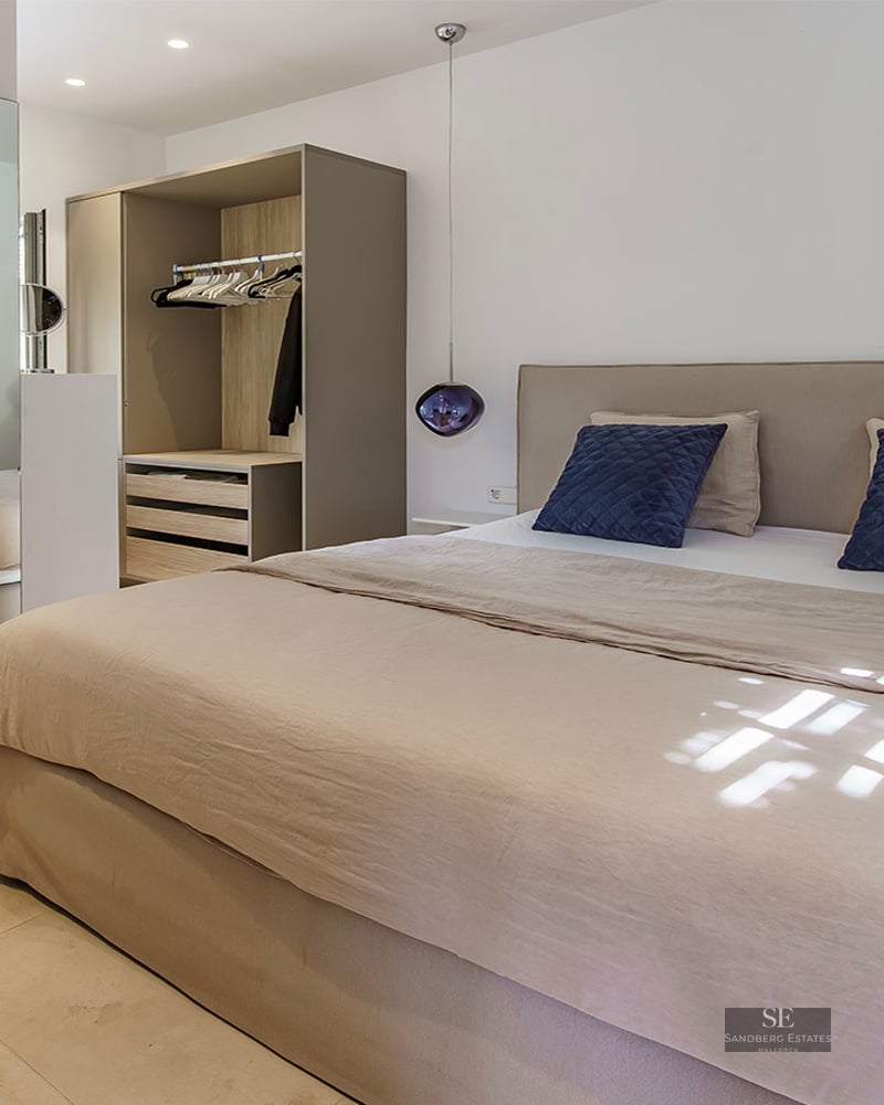 Bright modern bedroom featuring a beige bed, navy pillows, purple glass pendant lamps, and a built-in wardrobe with mirrors.