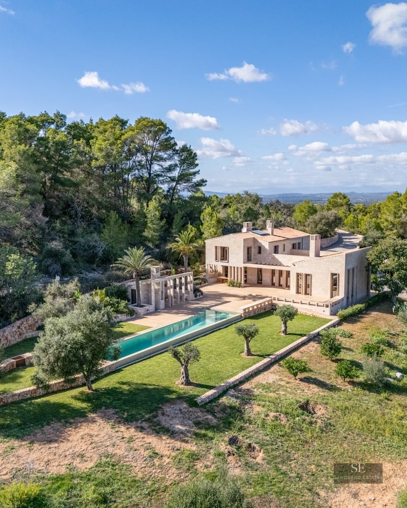 Aerial view of a luxury stone villa with a long turquoise pool surrounded by olive trees and lush forest.