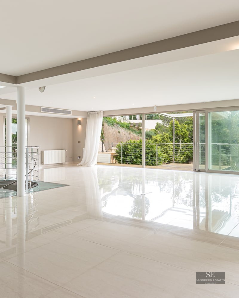 Spacious minimalist room with polished floors, a metal spiral staircase, and large glass doors leading to a terrace.