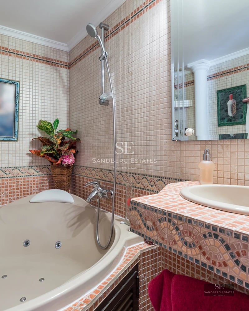 A bathroom with a whirlpool tub, a mosaic-tiled vanity with a sink, and warm-toned wall tiles.