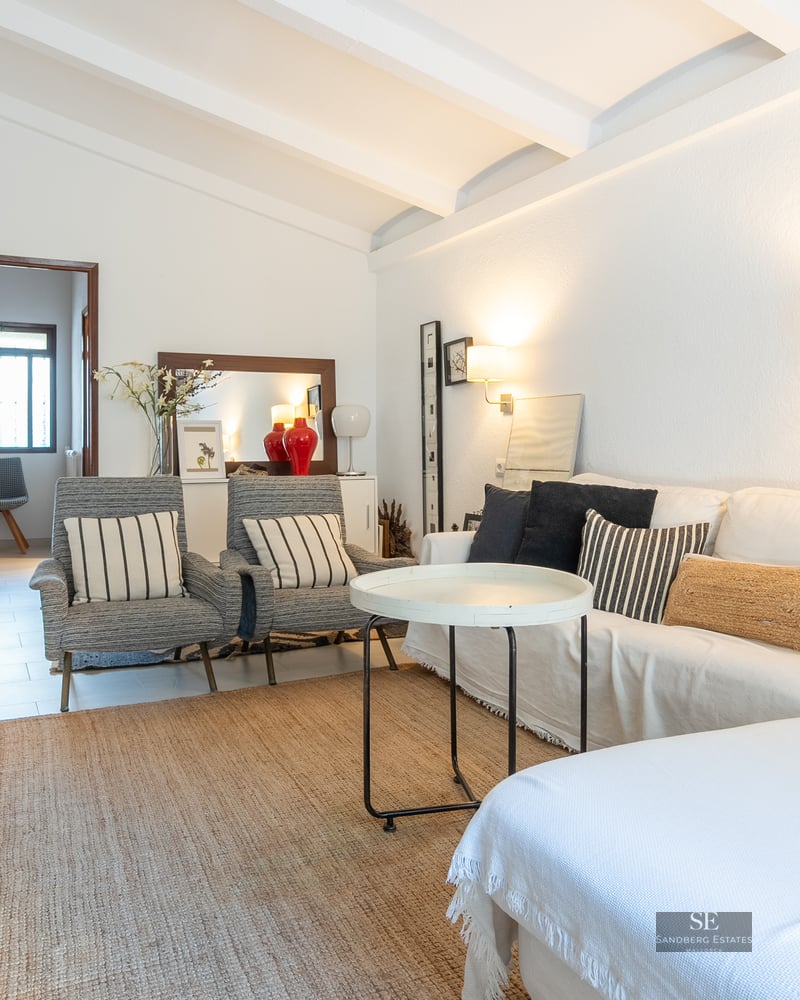 Bright living room featuring a white sofa, striped armchairs, a jute rug, and white exposed ceiling beams.