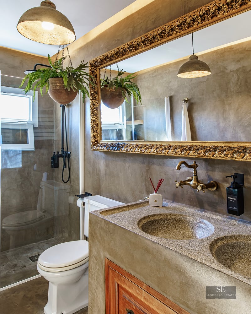 Luxury bathroom featuring microcement walls, an ornate gold mirror, double vanity, and glass shower enclosure.