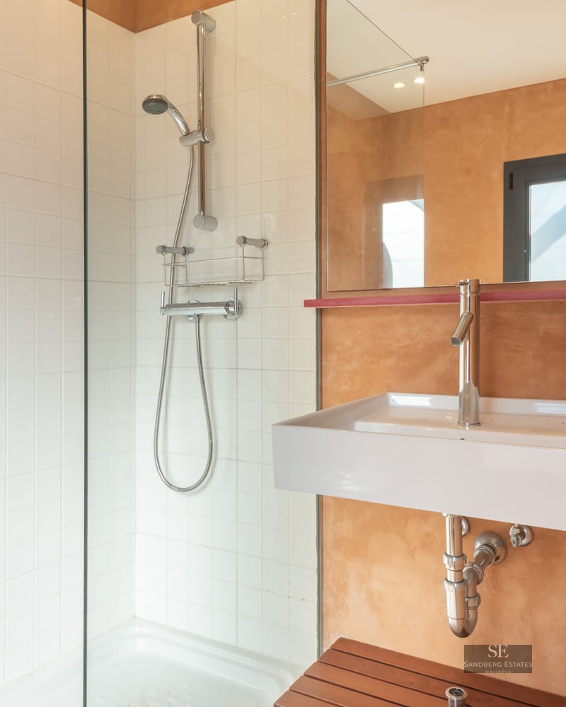 Modern bathroom featuring a walk-in glass shower, white square tiles, and warm terracotta textured walls with a white sink.
