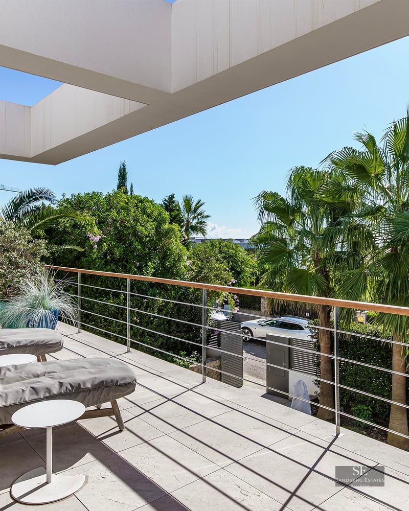 Grande terrasse moderne avec deux chaises longues grises surplombant des palmiers luxuriants sous un ciel bleu dégagé.