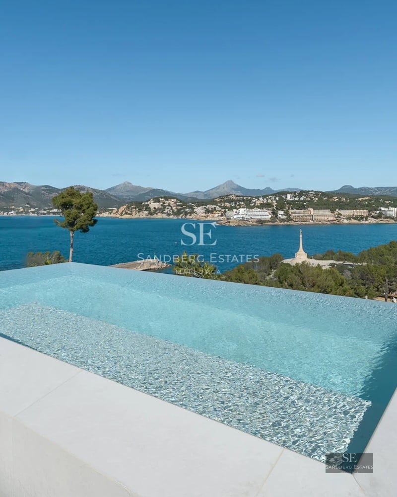 View of modern infinity pool with elegant sun loungers and lush vegetation. Minimalist architectural design.