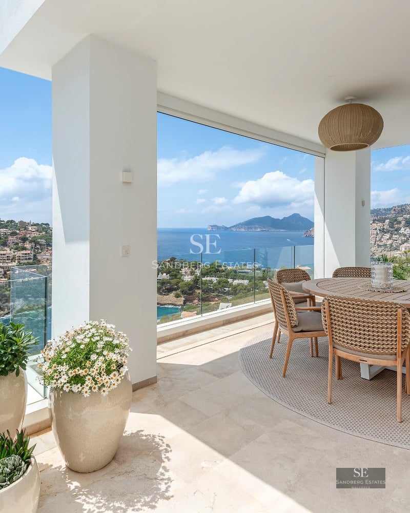 Spacious balcony with sea view. Glass railing, modern furniture, and light wood flooring. Relaxing and bright atmosphere.