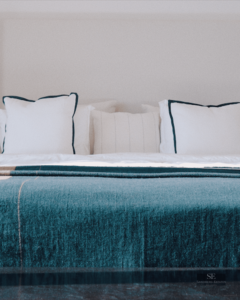 King-size bed with teal throw, symmetrical designer lamps, and wall mirrors in a luxury suite.