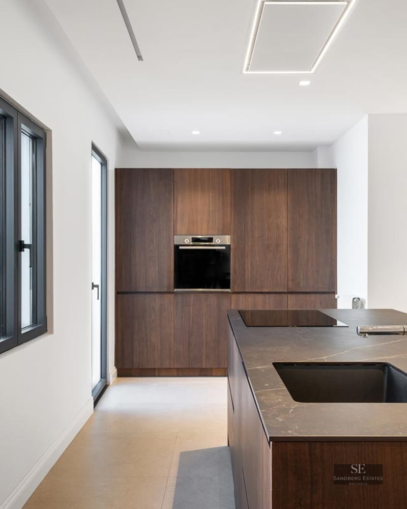 Modern kitchen featuring a dark wood island, black countertop, integrated sink, and full-wall built-in cabinetry.
