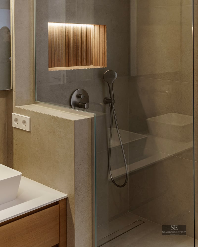 Salle de bain moderne avec vasque à poser, murs en pierre et douche vitrée avec niche en bois éclairée.