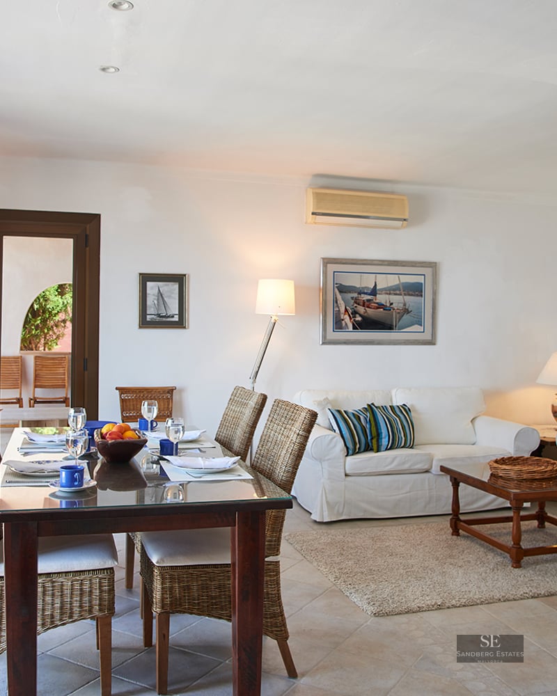 Spacious open-plan living room featuring white sofas, a wooden dining table, and wicker chairs under warm lighting.