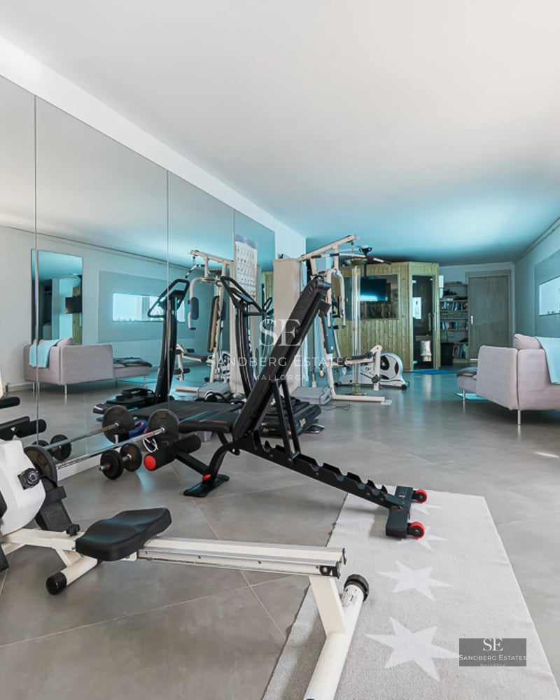 Reflecting pool with sundeck, loungers, and a modern house with large windows. Lush green environment and blue sky.