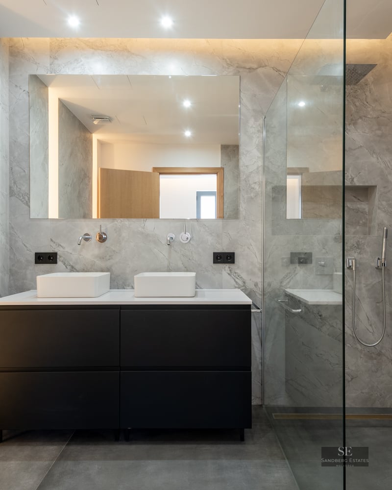 Elegant bathroom with gray marble walls, black double vanity, and glass walk-in shower.