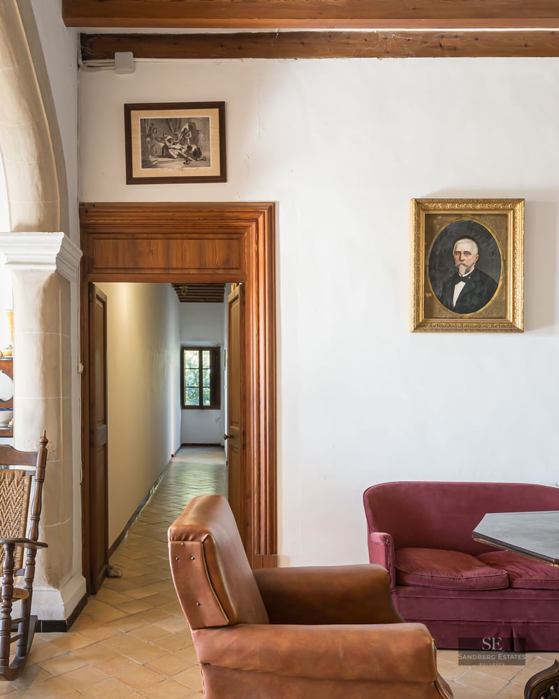 Classic living room with antique furniture, terracotta floors, red velvet sofa, and portraits on the walls.