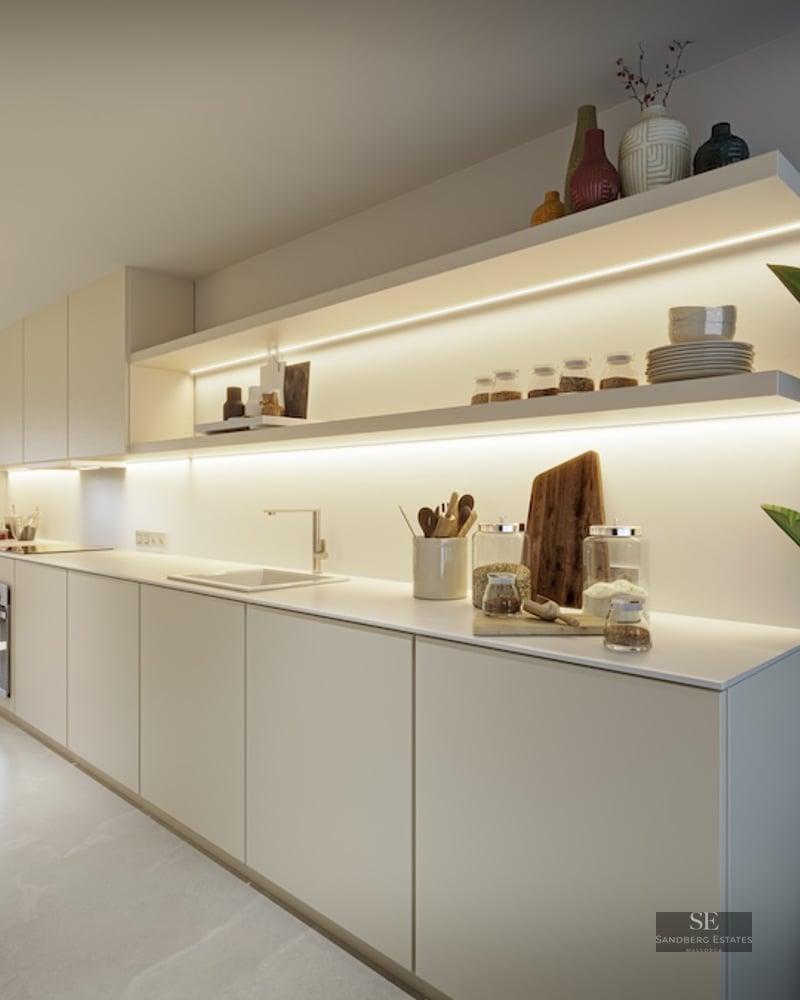 Modern beige kitchen featuring long countertops, open shelves with LED lighting, and a large indoor plant.
