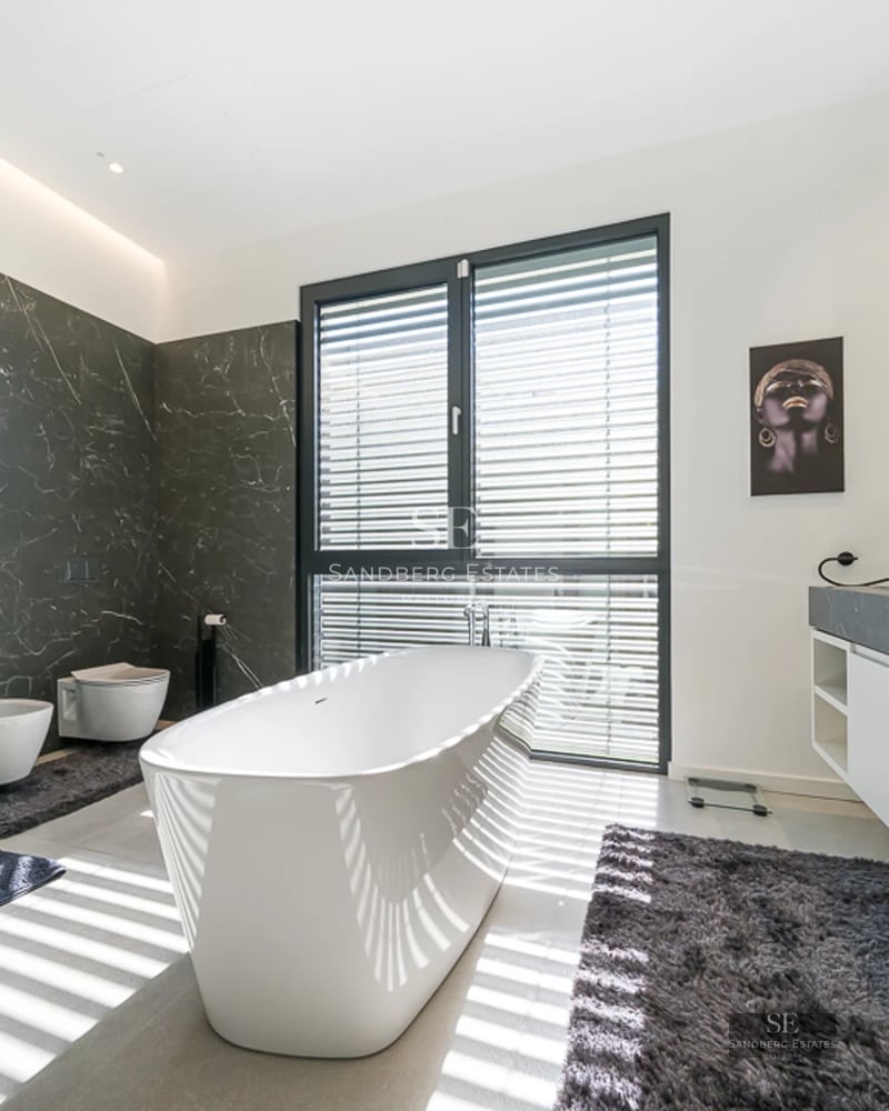 View of villa with infinity pool, sun loungers, and lush vegetation. Modern design with large windows and light colors.