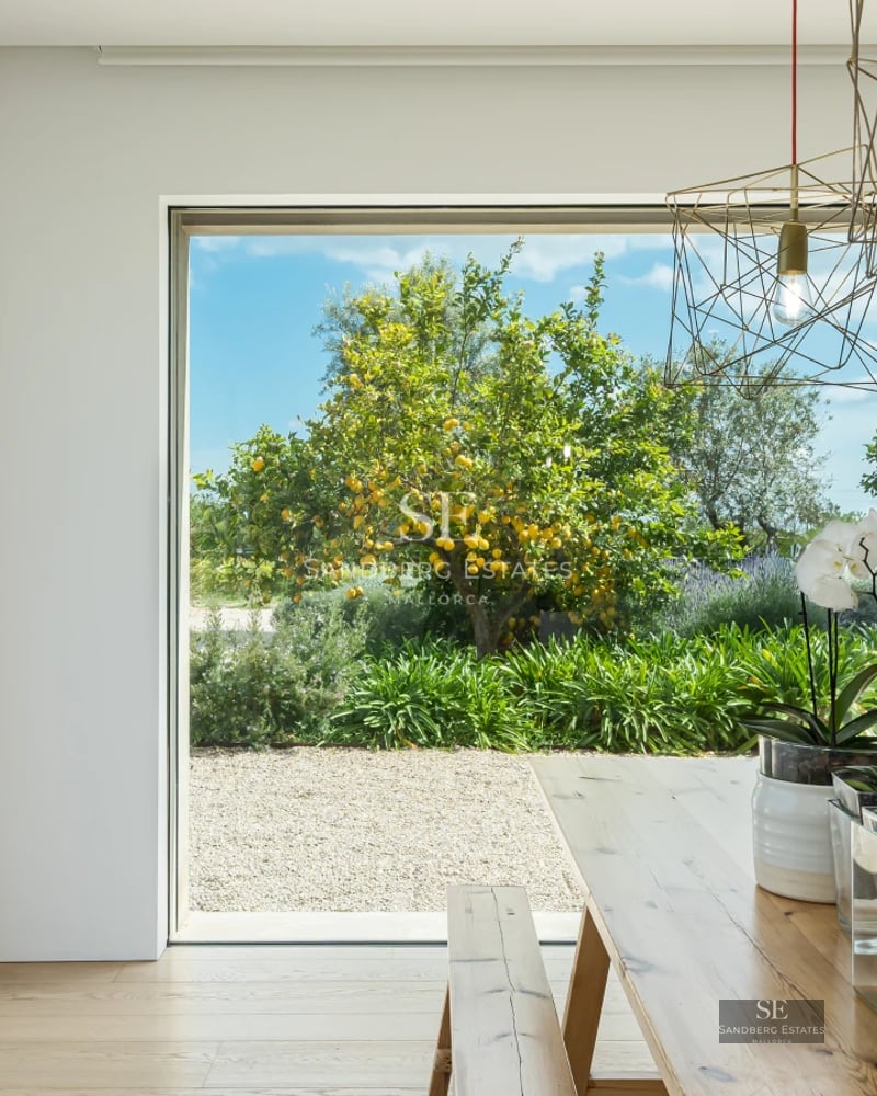 Modern living room with large windows, light wood flooring, grey sofas, and panoramic sea views. Abundant natural lighting.