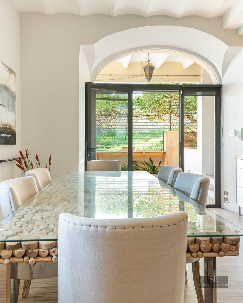 Bright dining room featuring a glass-top table with a rustic wood log base, white upholstered chairs, and an archway.