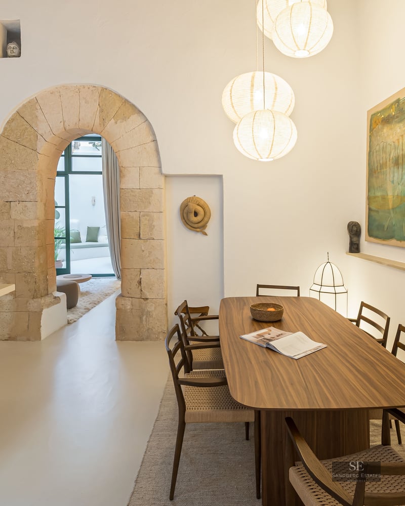 Modern wooden dining table under globe pendant lights, framed by authentic stone arches in a bright white space.