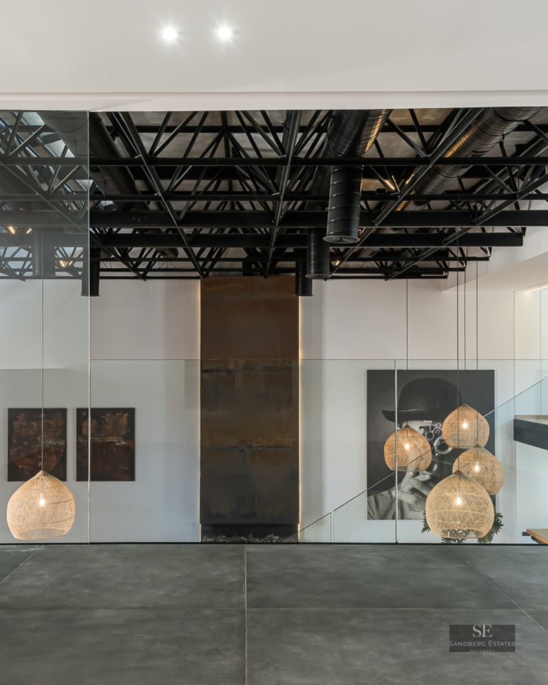 Modern interior featuring black steel ceiling trusses, glass railings, floating wood stairs, and designer pendant lamps.
